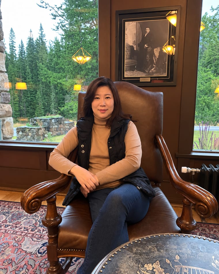 Judy seated in a quiet lodge sitting room looking out to the trees