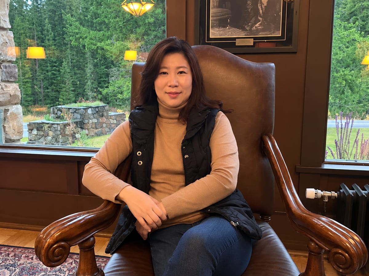 Judy seated in a leather armchair by a tall window looking out onto mountain pines